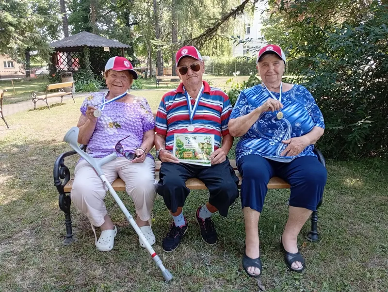 Tři seniorky s medailemi sedí na lavičce v parku